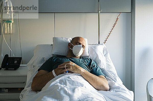 Patient mit Gesichtsschutzmaske schläft auf einem Bett im Krankenhaus