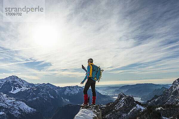 Älterer männlicher Wanderer  der sein Smartphone benutzt  während er auf dem Gipfel eines Berges steht  Orobic-Alpen  Lecco  Italien