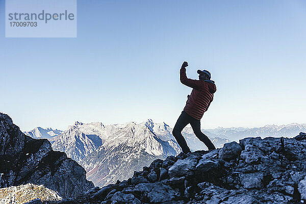 Sorgloser reifer Mann tanzt auf einem Berg gegen den klaren Himmel im Winter