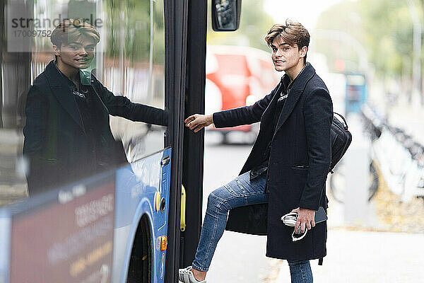 Hübscher junger Mann mit Rucksack beim Einsteigen in einen Bus in der Stadt
