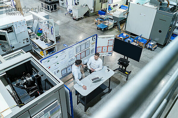 Männliche Kollegen mit Laptop auf dem Schreibtisch bei der Strategieplanung in einer Fabrik