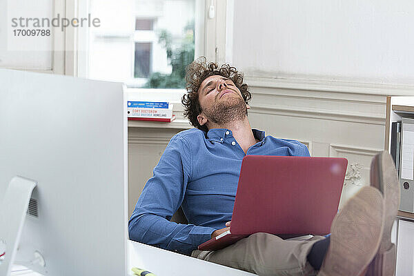 Junger Geschäftsmann schläft mit Laptop in Bürokabine