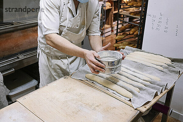 Männlicher Koch siebt Mehl aus einem Sieb auf den Teig in einer Bäckerei