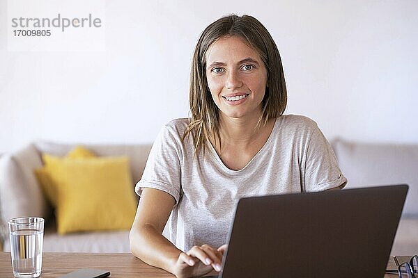 Lächelnde weibliche Fachkraft  die einen Laptop bei der Arbeit zu Hause benutzt