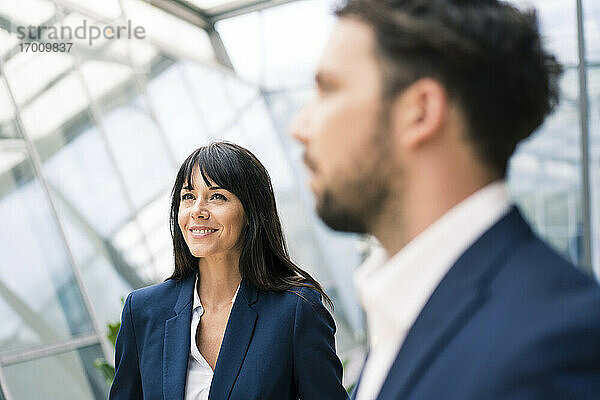 Lächelnde Geschäftsfrau  die neben einem männlichen Kollegen steht  der während einer Besprechung im Büro wegschaut