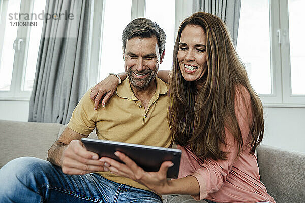 Lächelndes reifes Paar  das auf dem Sofa zu Hause ein digitales Tablet benutzt