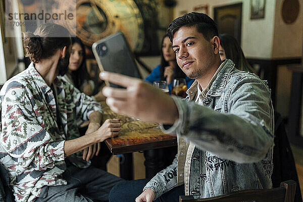 Junger Mann nimmt Selfie mit Freunden durch Mobiltelefon im Restaurant