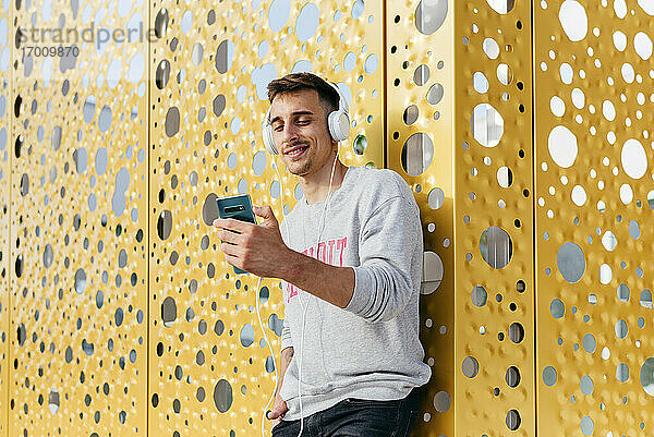 Lächelnder Mann hört Musik und lehnt sich an die Wand