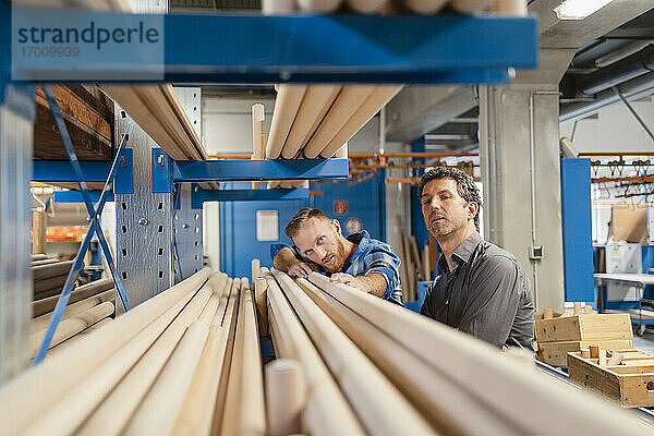 Zwei Zimmerleute prüfen Holzstangen in der Produktionshalle