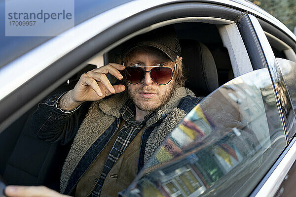 Mann mit Sonnenbrille  der wegschaut  während er im Auto sitzt  gesehen durch ein Fenster