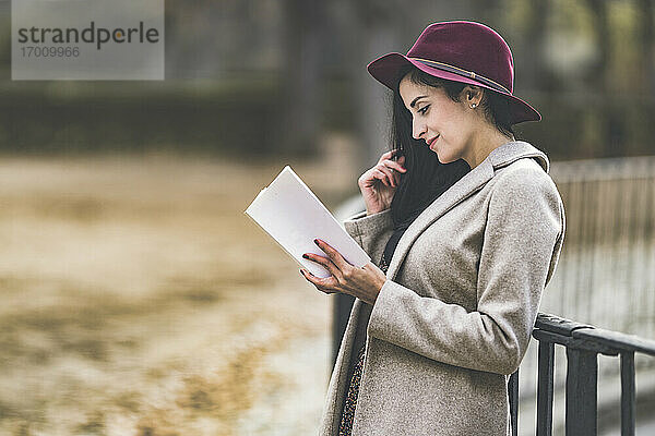 Schöne Frau mit Hut  die im Park steht und ein Buch liest