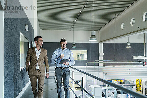 Männliche Kollegen mit digitalem Tablet auf dem Gehweg in einer Fabrik