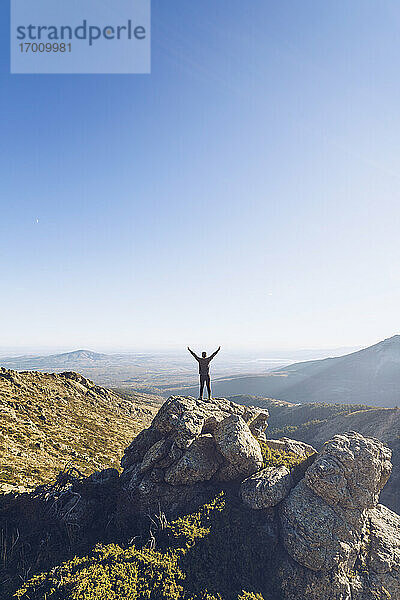 Männlicher Wanderer mit ausgestreckten Armen auf einem Berg stehend gegen den klaren Himmel