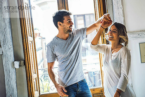 Glückliches junges Paar tanzt am Fenster zu Hause