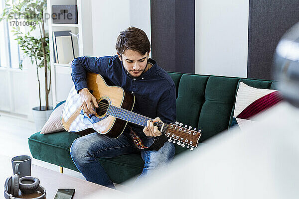 Musiker spielt Gitarre  während er auf dem Sofa im Studio sitzt