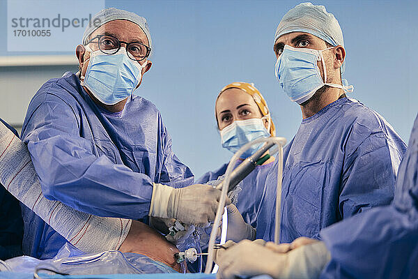 Chirurgen mit Gesichtsschutz bei arthroskopischen Eingriffen an der Schulter  während sie im Operationssaal stehen  während COVID-19