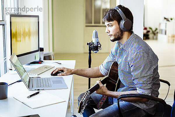 Profi mit Kopfhörern und Gitarre am Laptop im Aufnahmestudio