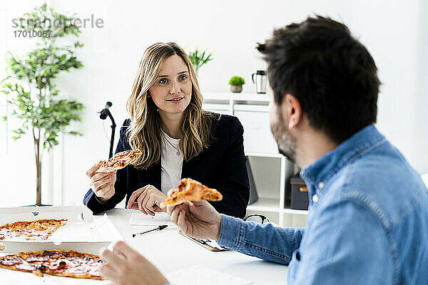 Geschäftsleute essen Pizza und unterhalten sich während der Pause im Büro