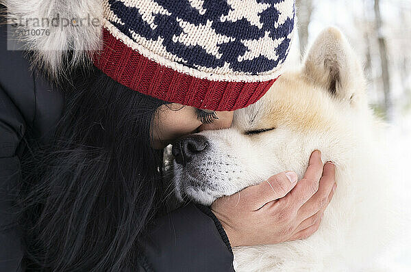 Mittlere erwachsene Frau küsst Akita-Hund im Winter