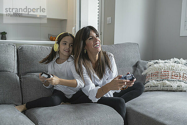 Lächelnde Mutter und Tochter spielen zu Hause zusammen Videospiele