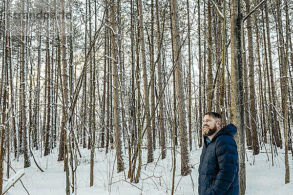 Lächelnder Mann in warmer Kleidung  der beim Spaziergang im Wald wegschaut