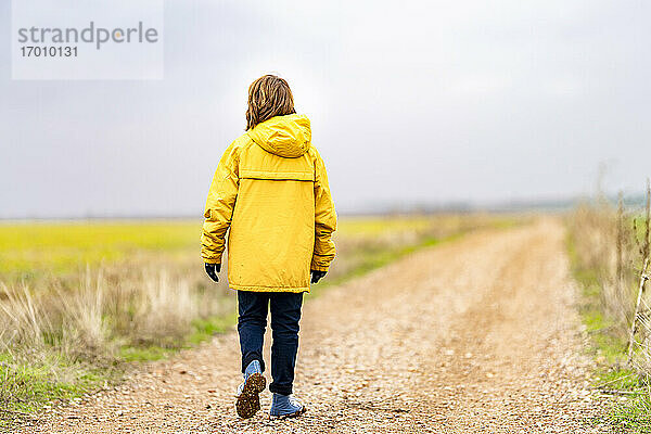 Junge in gelber Jacke geht leeren Feldweg entlang