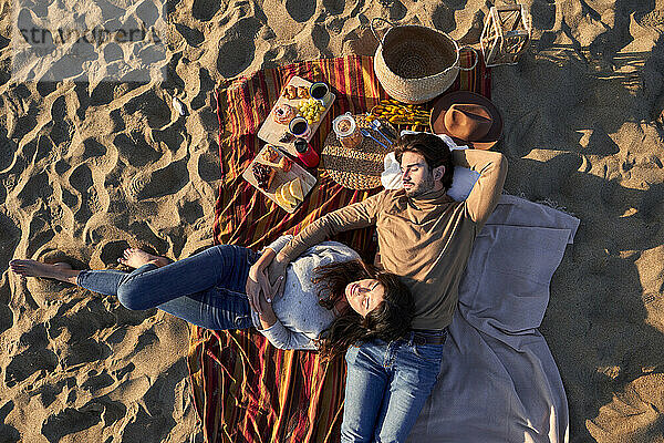 Freundin und Freund liegen auf einer Decke und ruhen sich am Strand aus
