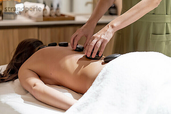 Massagetherapeutin legt Steine auf den Rücken einer Kundin im Schönheitssalon