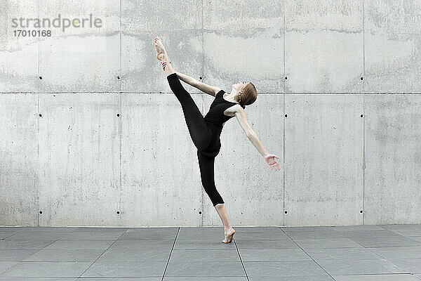 Tänzerin im schwarzen Trikot tanzt vor einer Betonwand