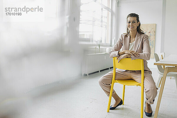 Porträt einer lächelnden Geschäftsfrau  die auf einem Stuhl im Büro sitzt