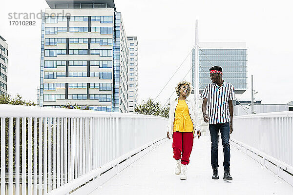 Mittlere erwachsene Frau und Mann unterhalten sich beim Gehen auf einer Brücke in der Stadt