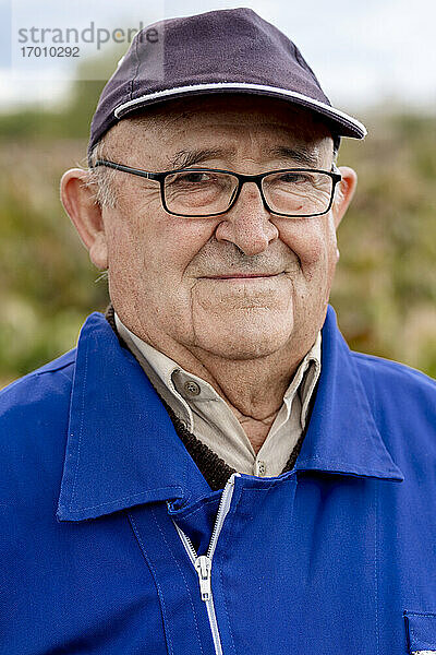 Älterer Mann mit Mütze und Brille vor einem Weinbauernhof