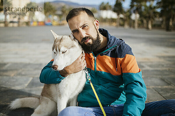 Bärtiger Mann umarmt Siberian Husky auf der Straße sitzend