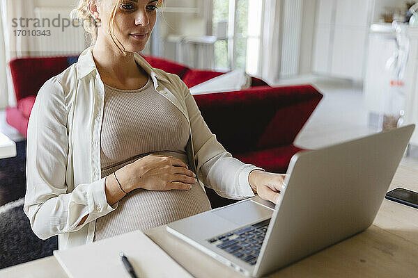 Schwangere Freiberuflerin mit Laptop im Wohnzimmer