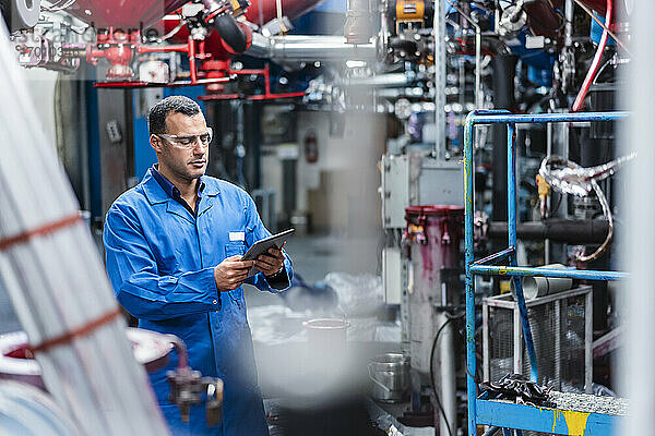 Männlicher Techniker  der ein digitales Tablet bei der Arbeit in einer Fabrik benutzt