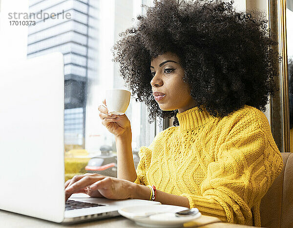 Junge Frau trinkt Kaffee und arbeitet am Laptop in einem Café