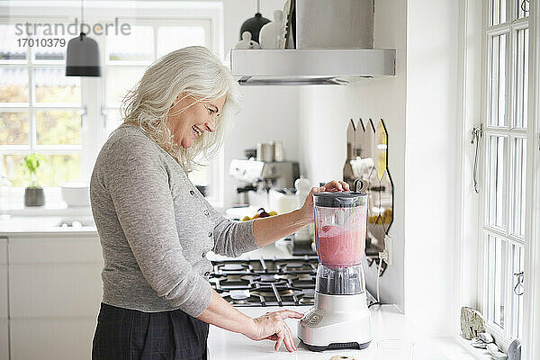 Glückliche Frau im Ruhestand bereitet Erdbeer-Smoothie in der Küchenmaschine zu