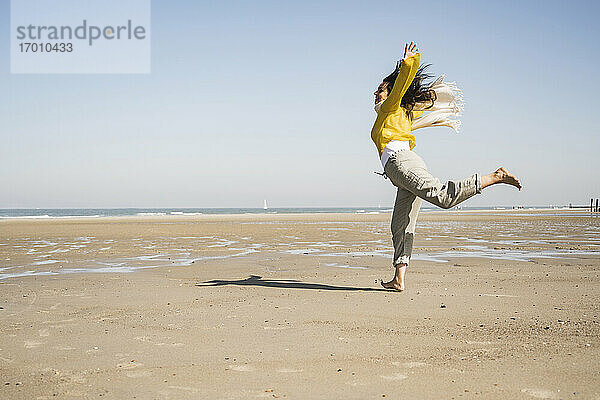 Unbekümmerte Frau springt am Strand gegen den klaren Himmel an einem sonnigen Tag