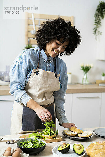 Porträt einer jungen Frau  die in der Küche vegane Sandwiches zubereitet