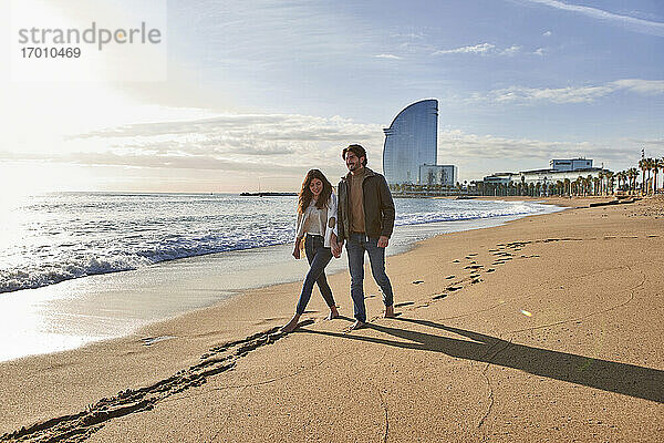 Freundin und Freund halten sich an der Hand  während sie am Strand spazieren gehen