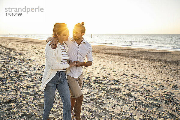 Junges Paar hält sich an den Händen  während es an einem sonnigen Tag am Strand spazieren geht