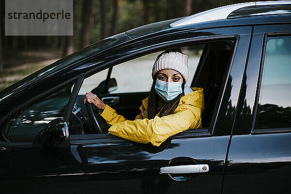 Frau mit gelbem Regenmantel und Gesichtsmaske sitzt im Auto