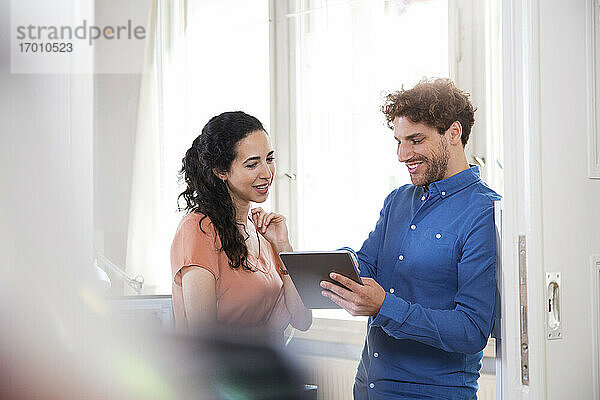 Lächelnder Geschäftsmann  der ein digitales Tablet benutzt und neben einer Kollegin im Büro steht