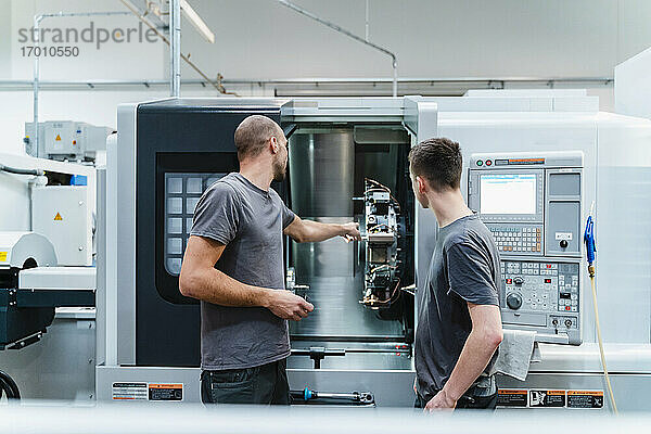 Ingenieur zeigt einem Auszubildenden ein Maschinenteil bei der Arbeit in der Industrie