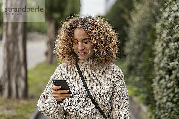 Lächelnde junge Frau  die mit ihrem Smartphone in der Stadt Textnachrichten verschickt