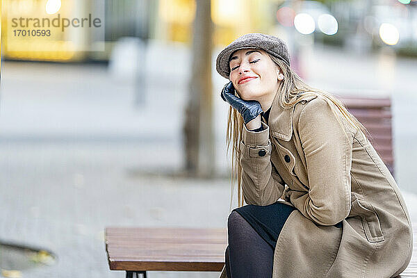Lächelnde Frau  die auf einer Bank am Fußweg sitzt und träumt