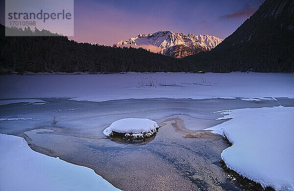 Strom fließt auf schneebedecktem Land gegen Berg bei Sonnenuntergang