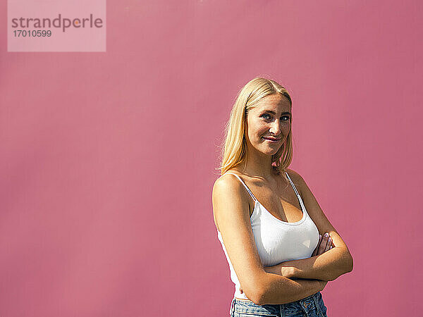 Lächelnde schöne Frau mit verschränkten Armen vor einer rosa Wand