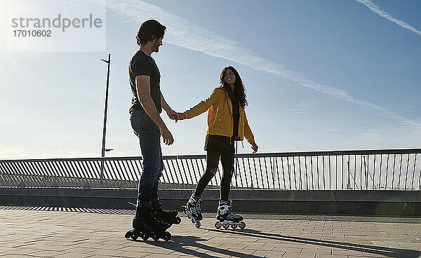 Glückliches junges Paar hält sich beim Schlittschuhlaufen auf dem Pier an den Händen