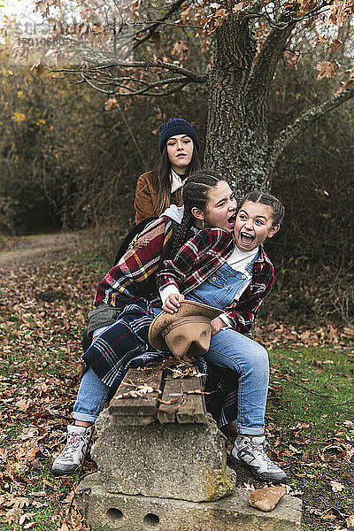 Drei lächelnde Schwestern auf einer Bank in einer Herbstlandschaft